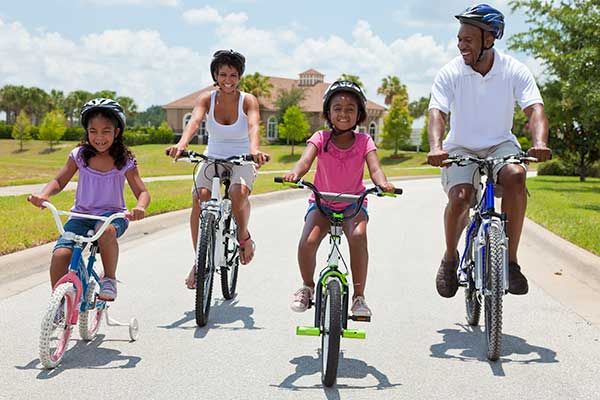 A family rides bicycles through a residential neighborhood on a sunny day.